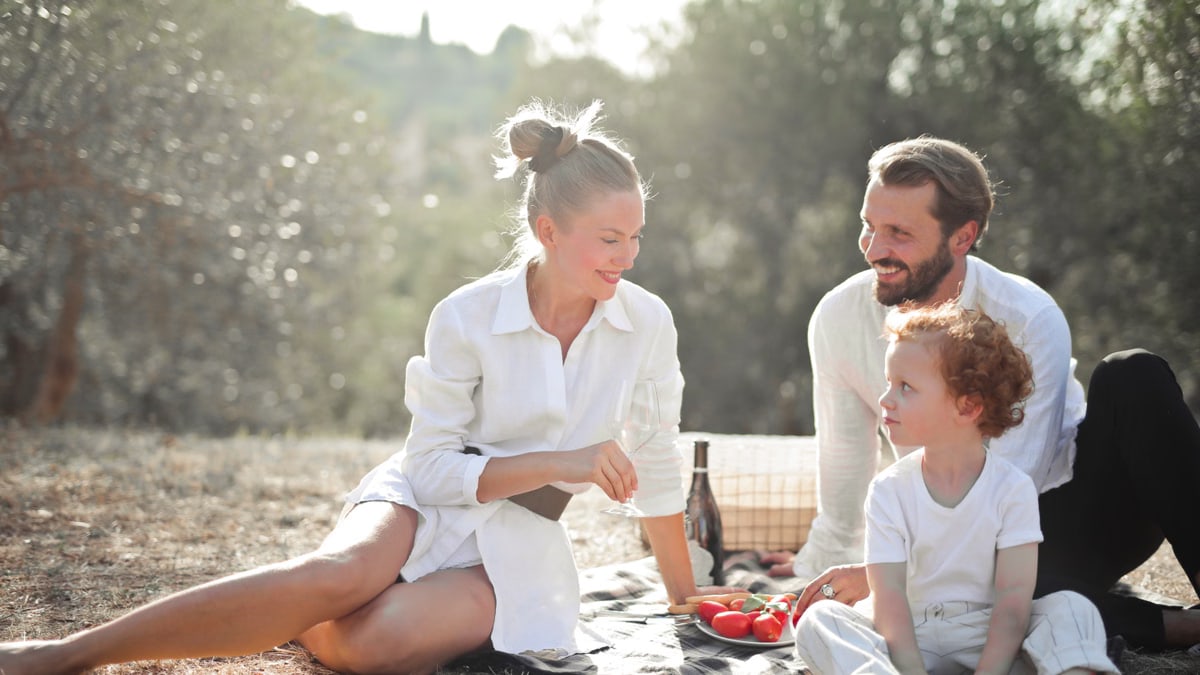 A cheerful family enjoying a picnic outdoors with smiles and sunny skies.