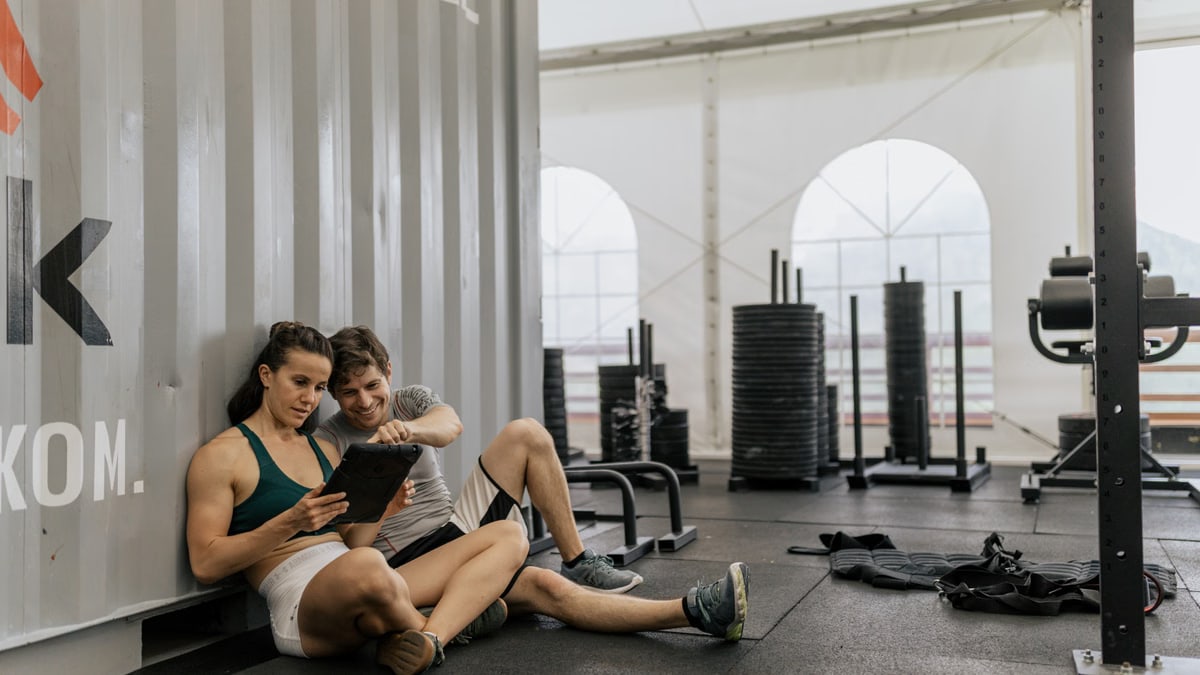 A young couple sitting on the gym floor, using a tablet in a modern urban fitness center.